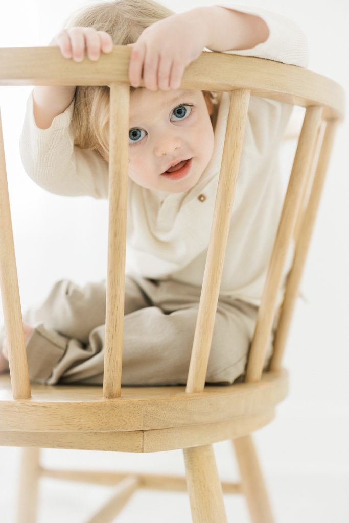 two year old boy looking through back of chair at photographer by NYC Family Photography