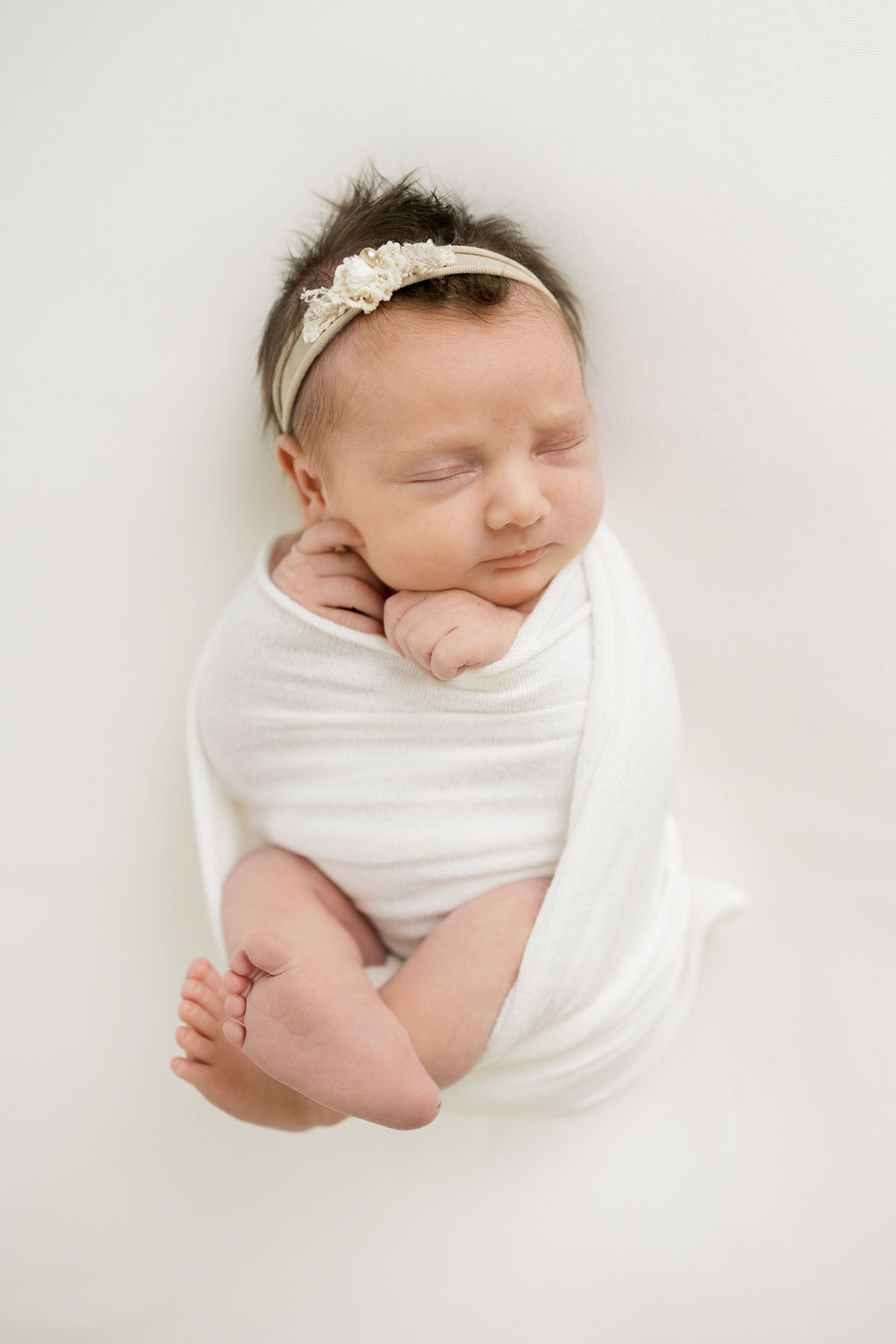 newborn baby wrapped in a white swaddle with a flower bow baby crossing