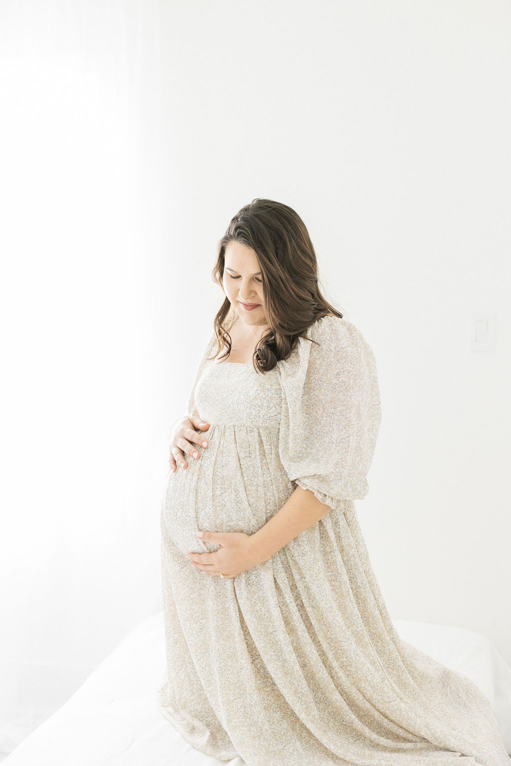 mom to be in cream maternity gown cradling her bump in a studio
