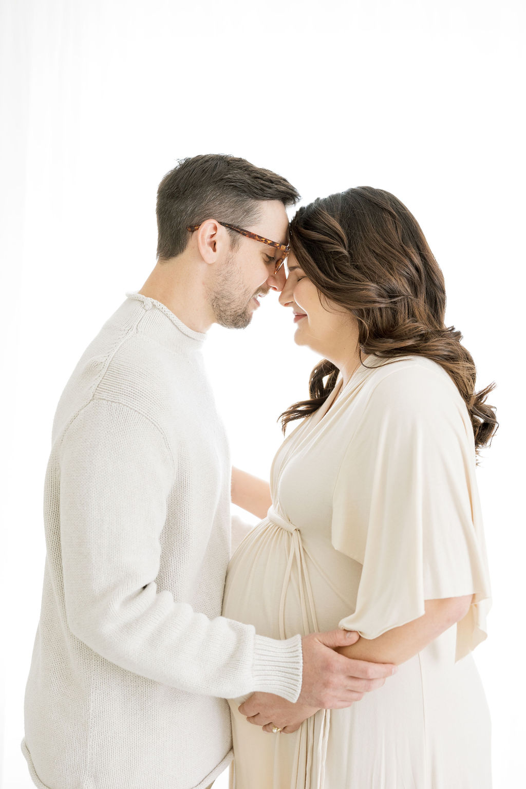 mom and dad to be in cream outfits cradling their baby bump doula morristown nj