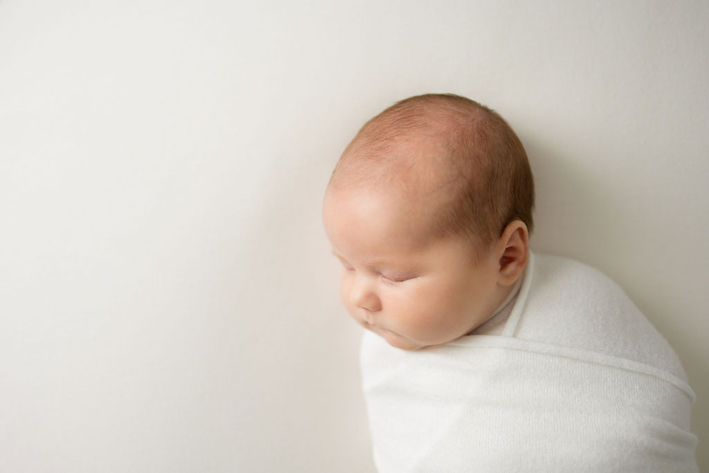 Newborn baby sleeps in a white swaddle in a studio