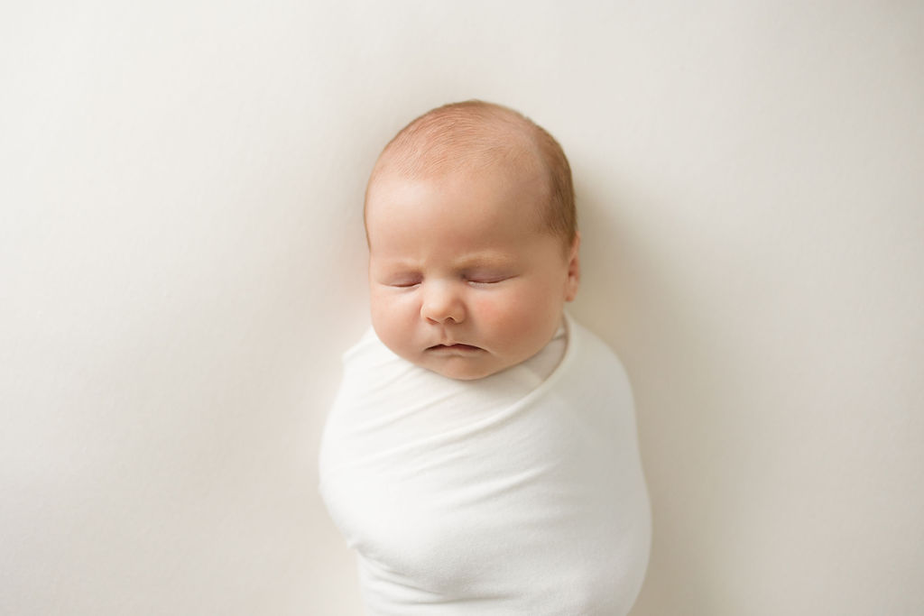 Newborn baby sleeps swaddled in a white blanket in a studio swaddles baby teaneck nj
