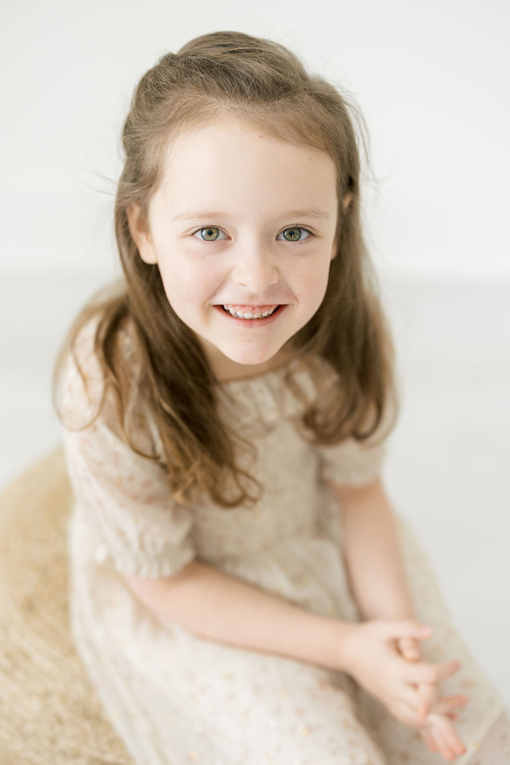 Girl wearing a beige dress sits on a woven stool in a studio Carriage Boutique