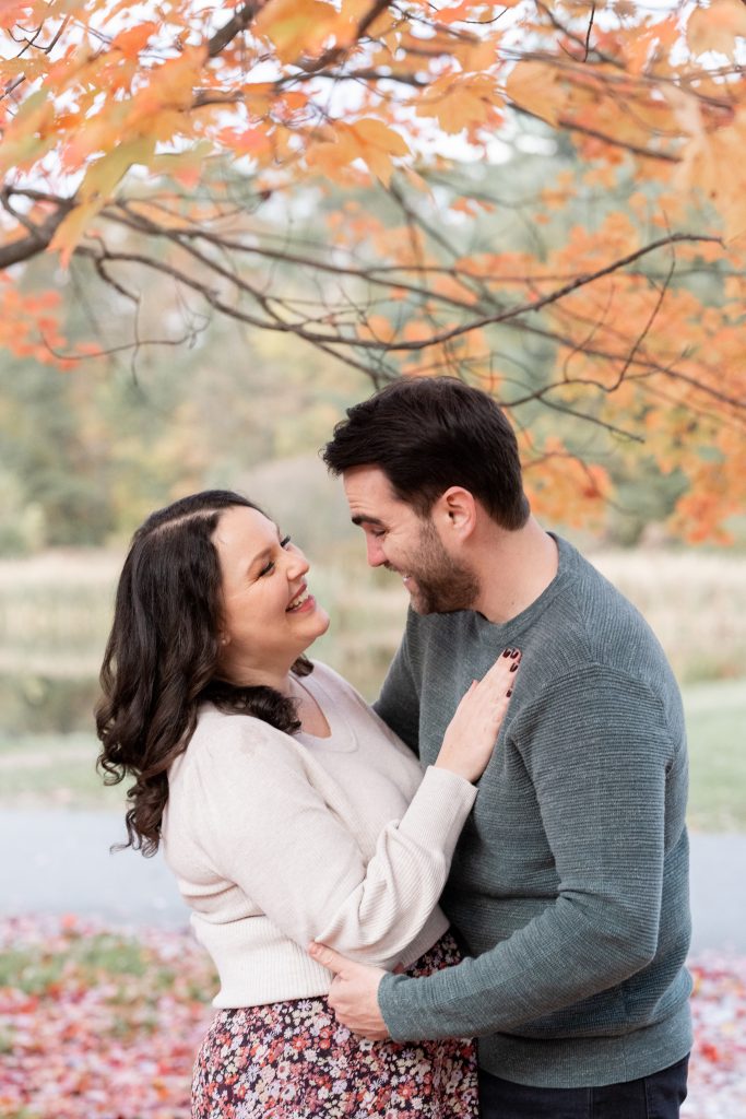 husband and wife under fall foliage hugging and laughing by NYC Family photographer