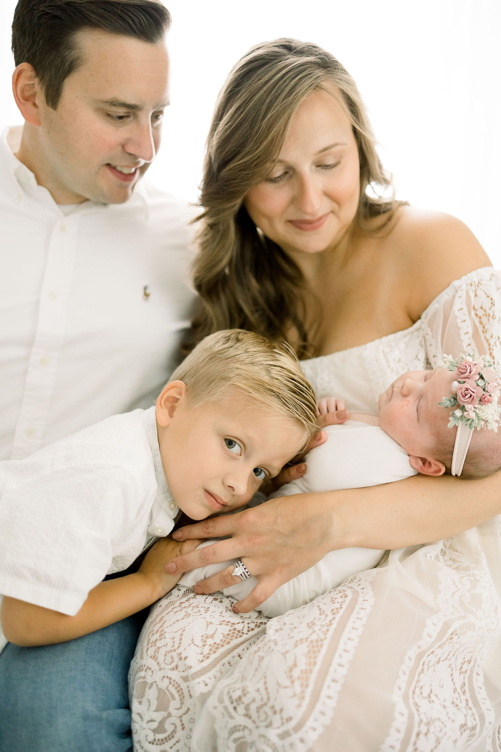 Mother in a white lace dress holds her newborn while older brother rests head on her hand max and luna