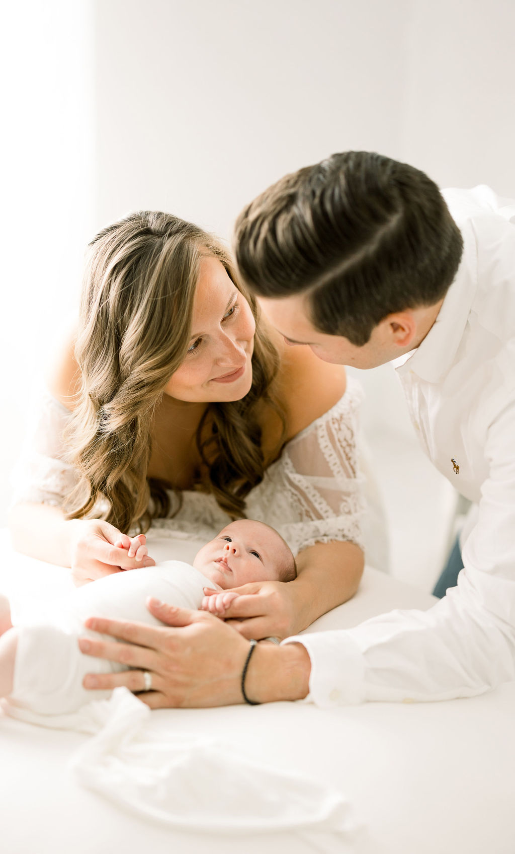 mother and father look at each other while playing with newborn baby mindful birth