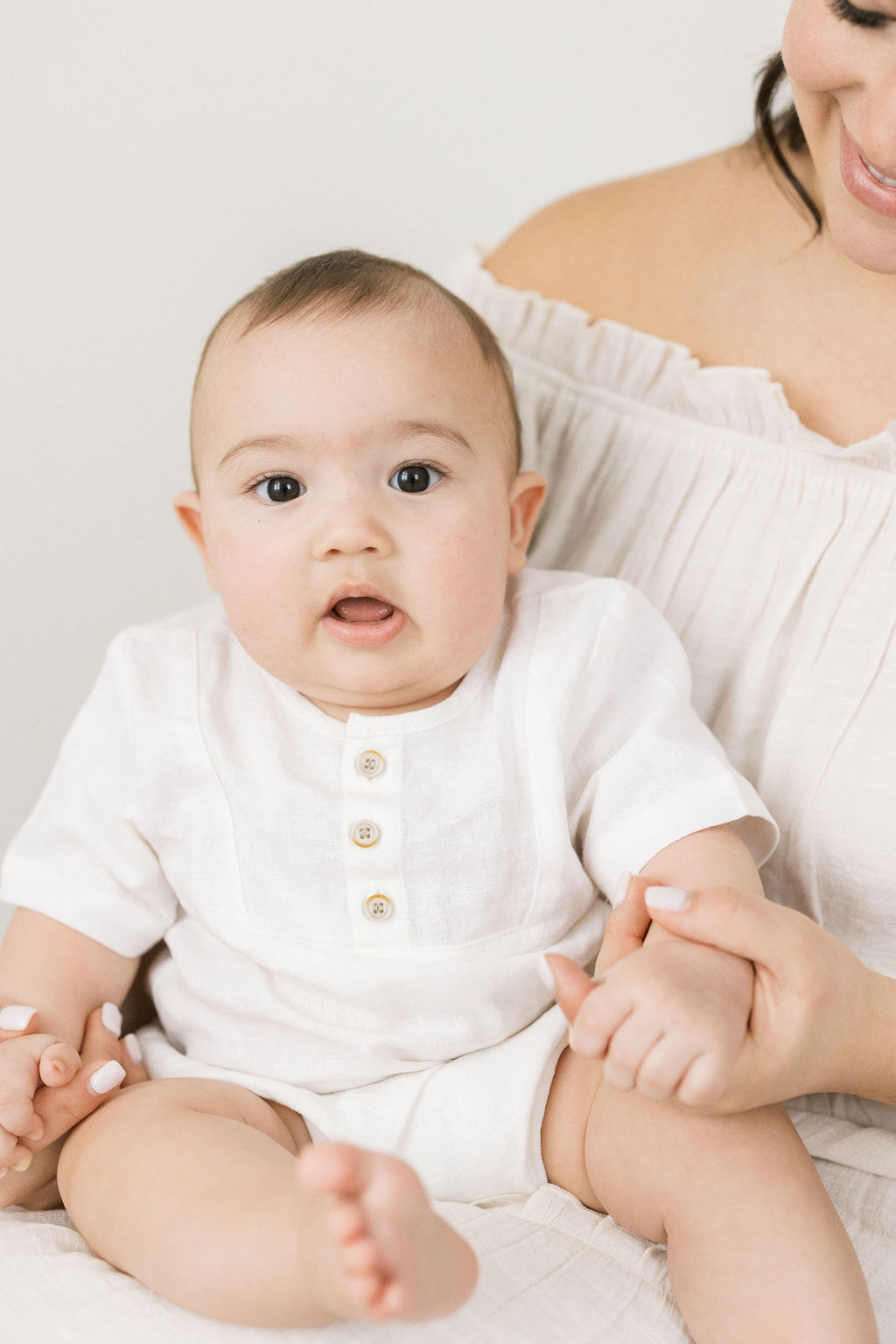 mother plays with her toddler in a white dress and white henley shirt