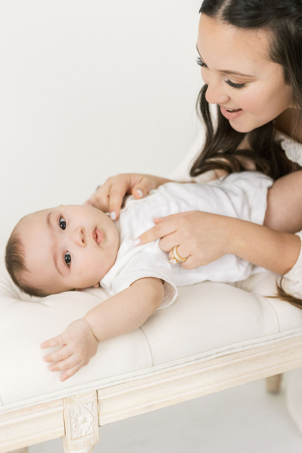 mother plays with her newborn baby on a beige bench in a studio montclair baby