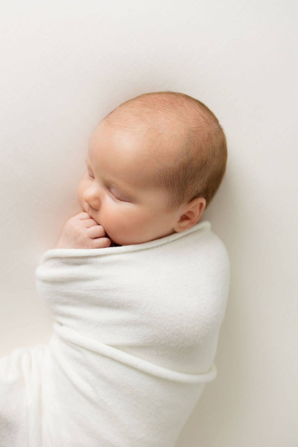 Newborn baby sleeps with fingers curled under mouth in a studio precious faces in 3D