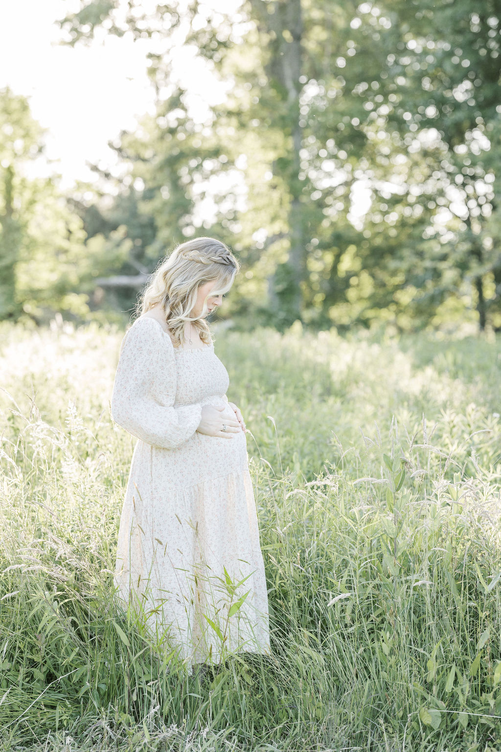 Mother to be stands in tall grass while looking down at her hands on her bump prenatal massage morristown nj