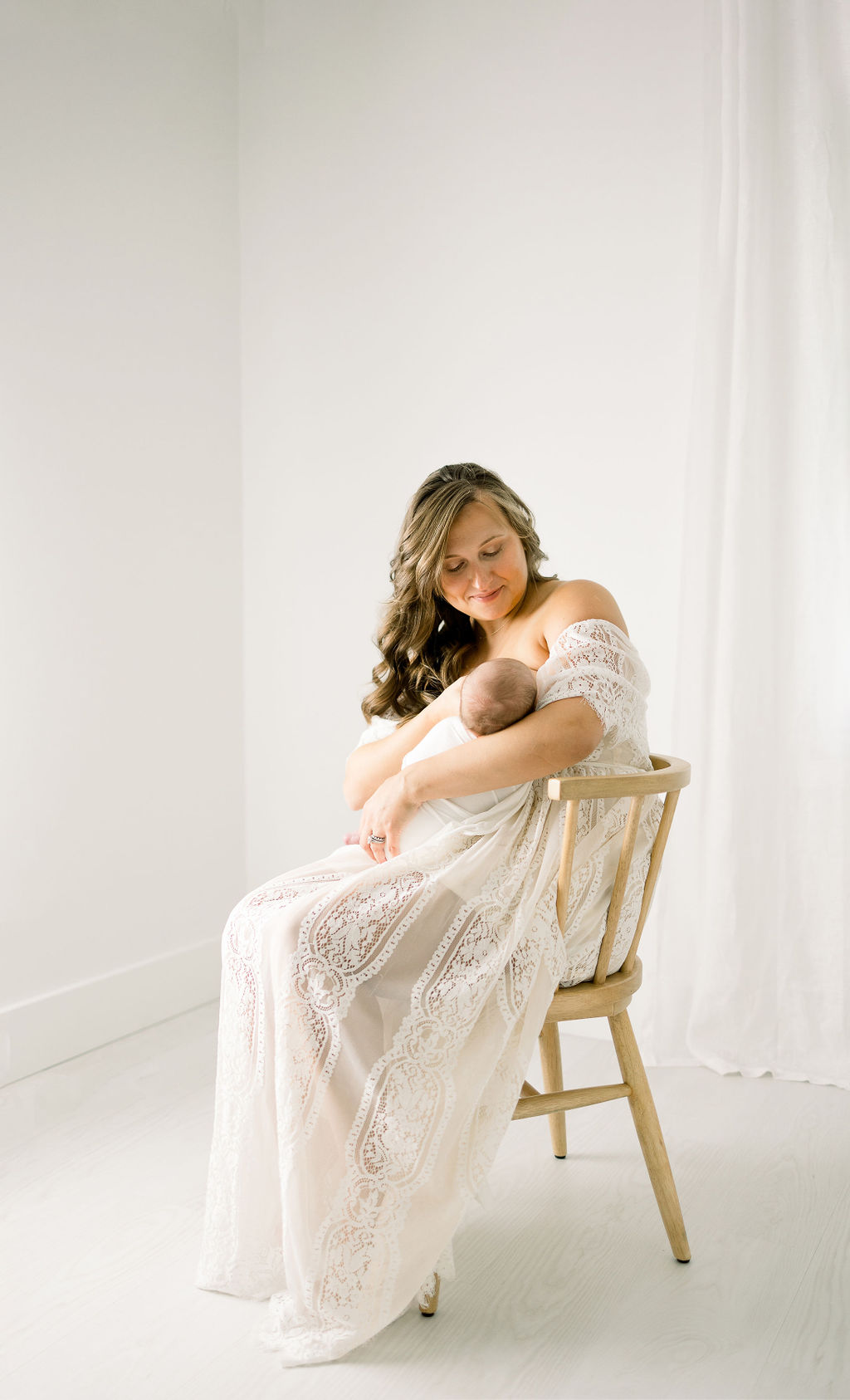 Mother sits in a wooden chair in a studio while breastfeeding her newborn baby swaddles baby teaneck nj
