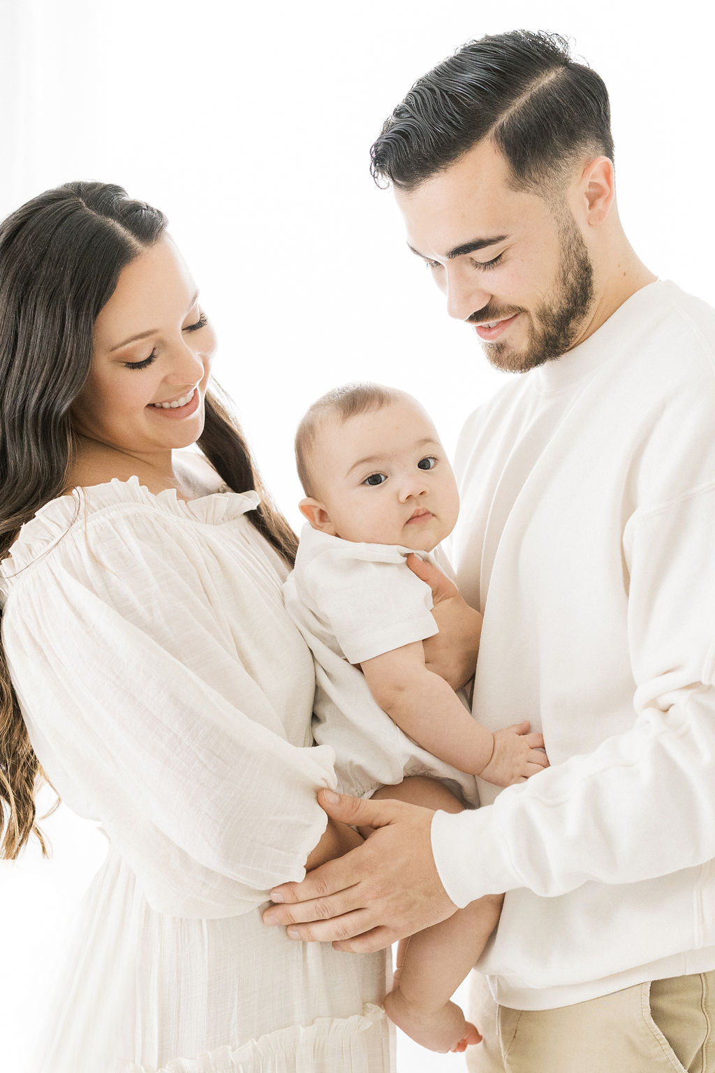 Mom and dad both in white hold their young son in between them