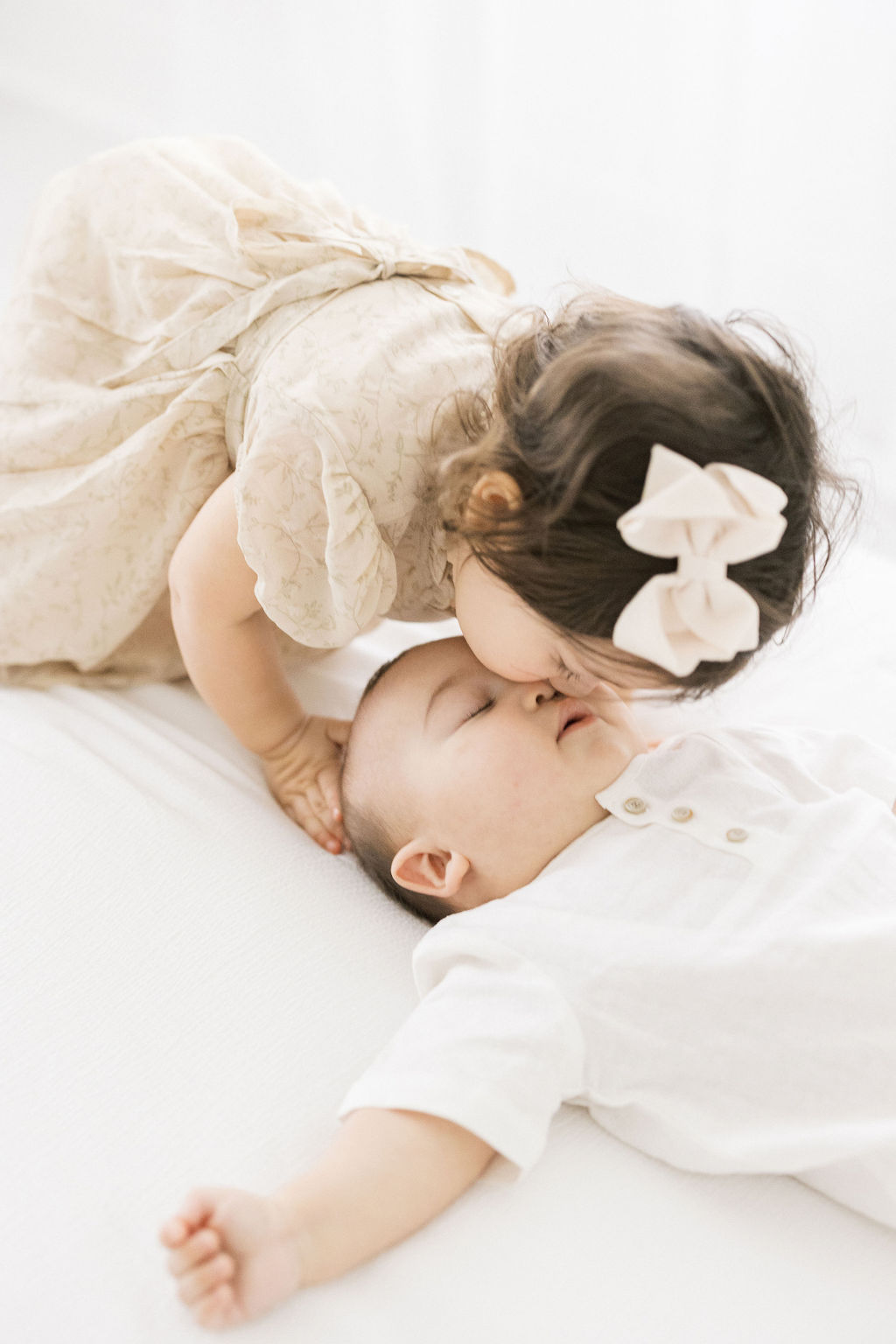 A sleeping newborn baby gets a kiss on the head from their older sister in a beige dress and bow sage midwifery nj