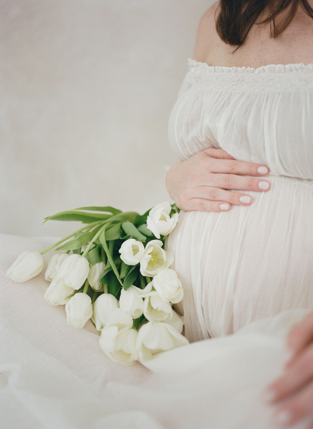 Details of a mom to be siting on a bed with white tulipschildbirth center clifton