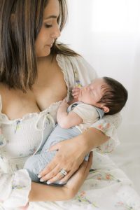 A new mother sits in a studio holding her newborn baby against her chest morristown pediatric dentist