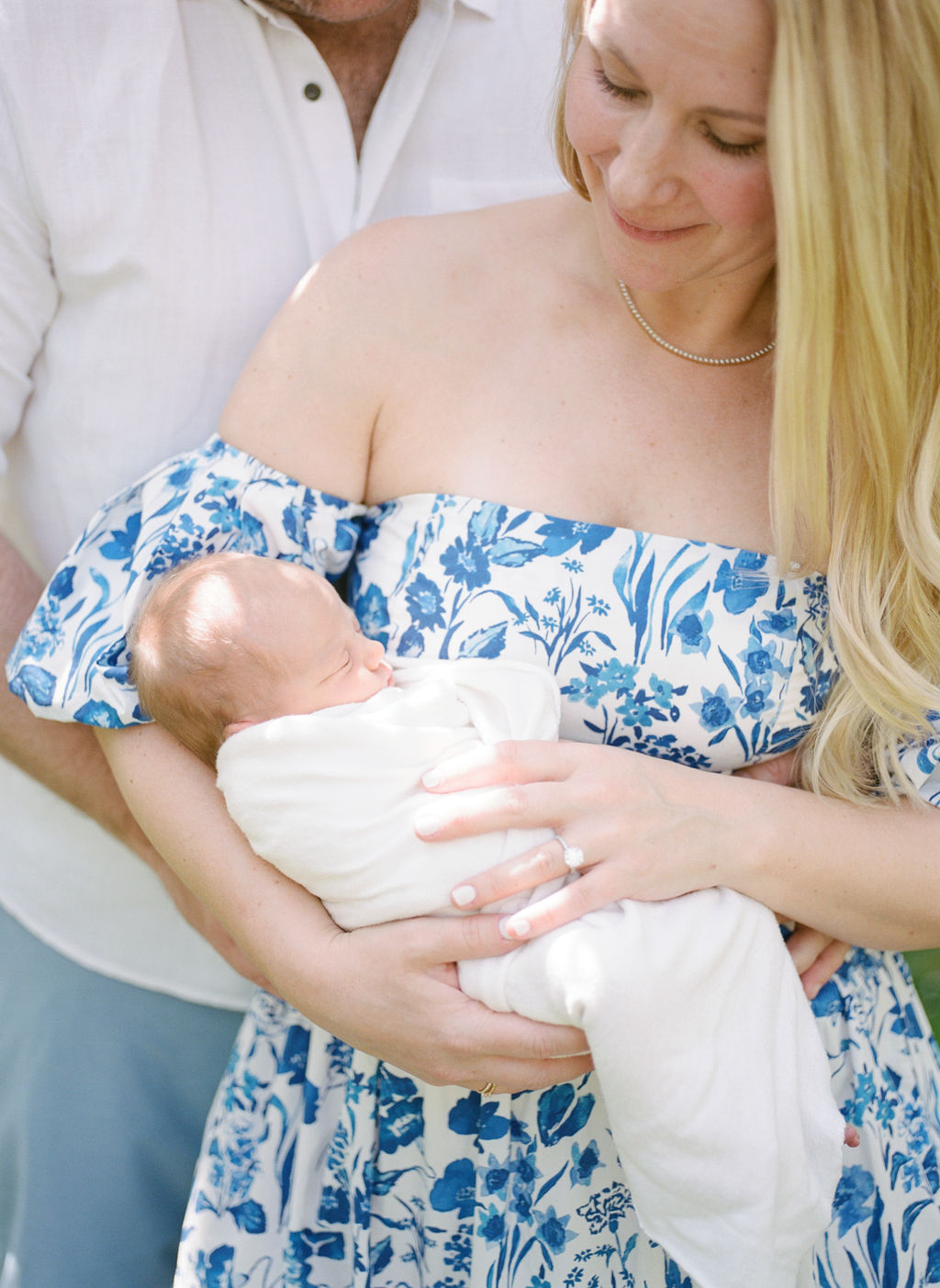 A mother looks down at the newborn baby in her arms while dad hugs her from behind