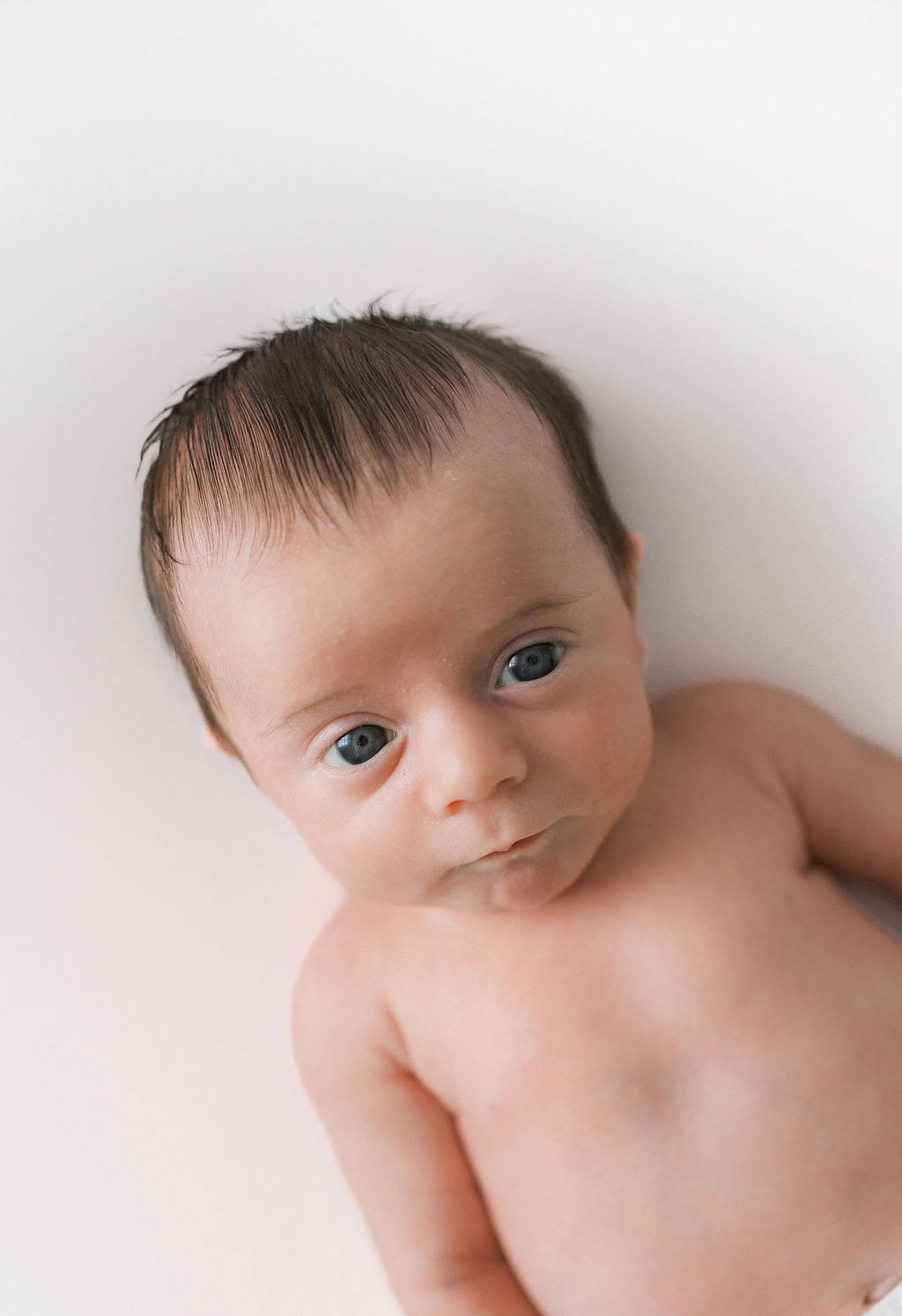 A newborn baby lays on a white cushion in a studio with eyes wide open overlook labor and delivery