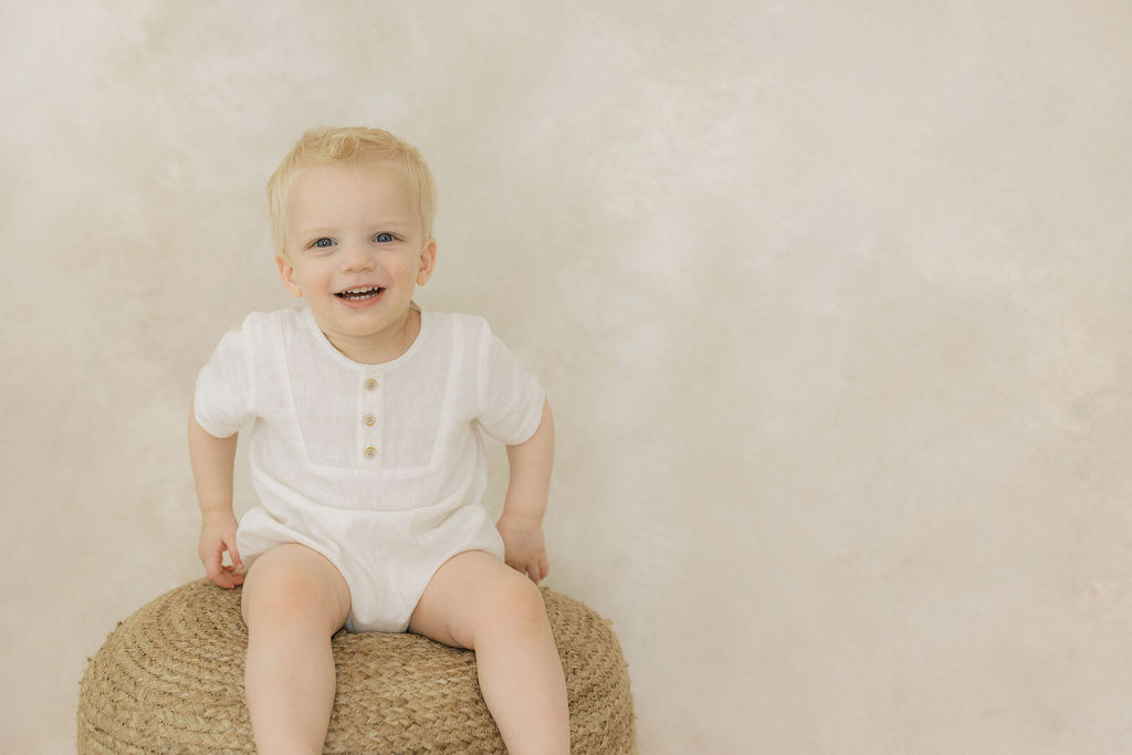 A young boy plays while sitting on a woven stool iin a studio