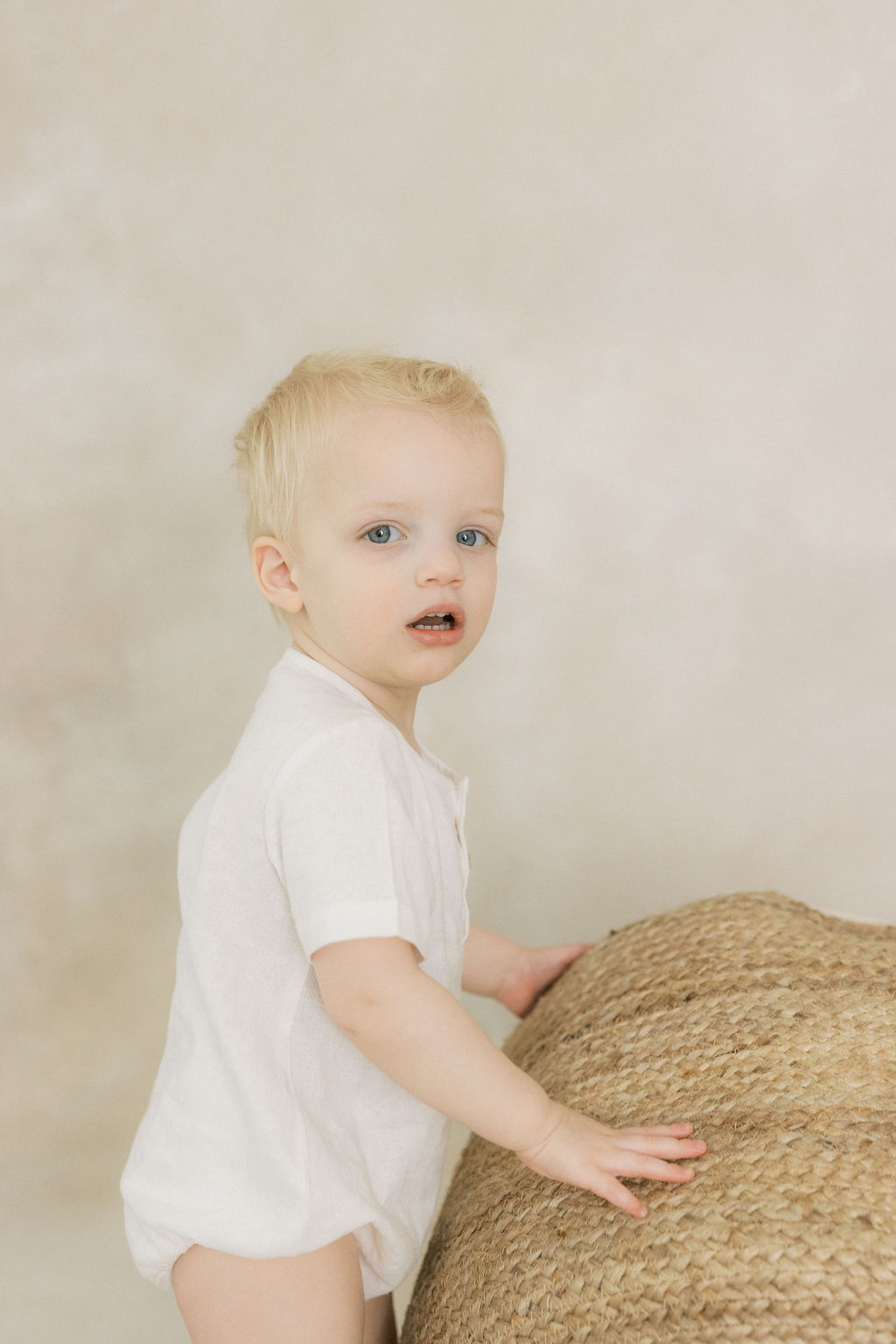 A young toddler with blonde hair and a white onesie plays with a woven basket in a studio baby furniture stores nj
