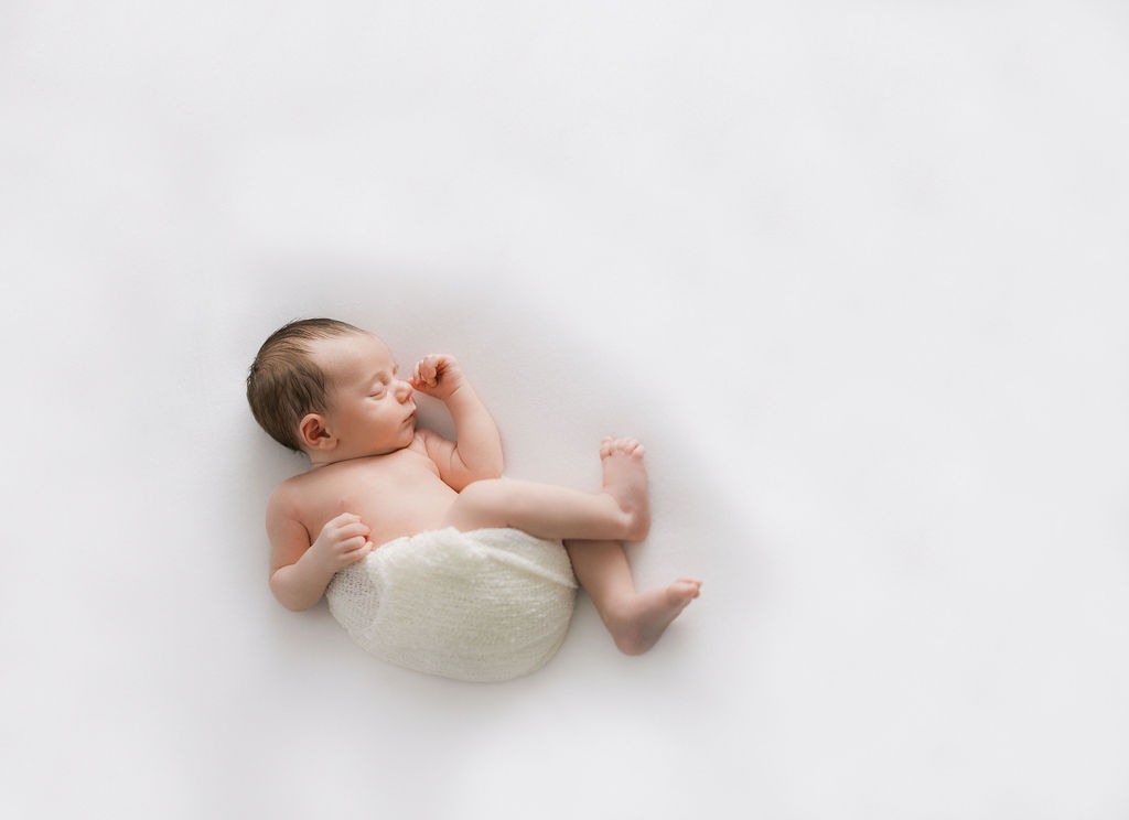 A newborn baby sleeps in a cheesecloth swaddle in a studio cuties boutique