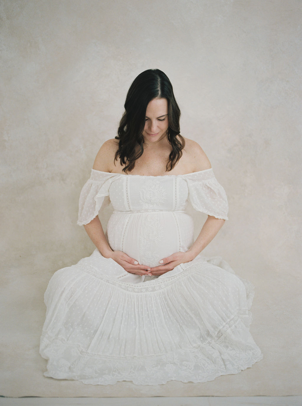 A mom to be looks down her bump while sitting with legs crossed in a studio prenatal yoga bergen county
