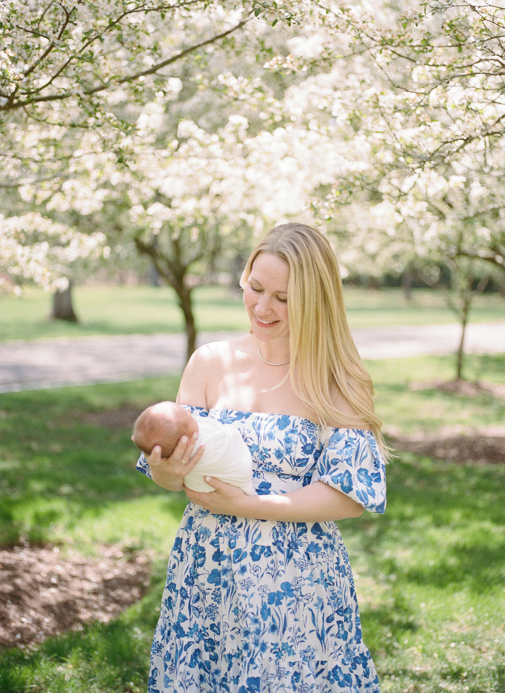 A new mother holds her newborn baby in front of her under white blooming trees