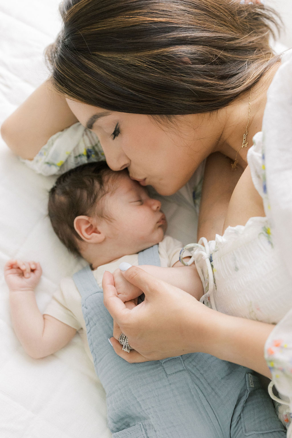 A mother lays with and kisses her sleeping newborn baby on a bed mommy and me classes nj
