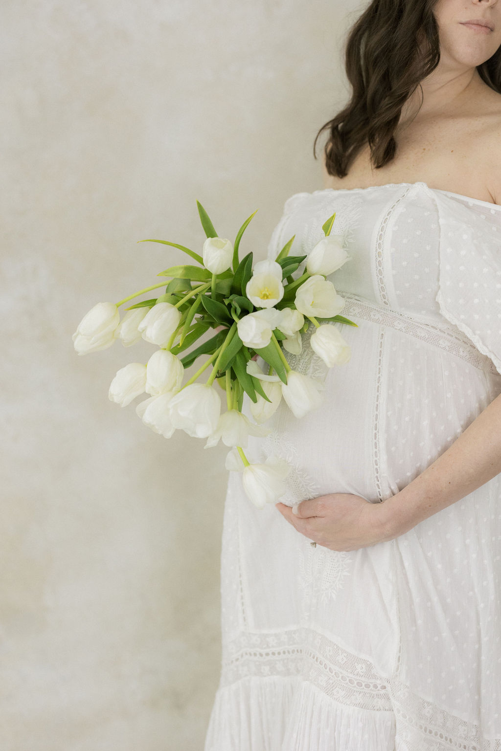 Details of a mother to be holding her bump and white tulips while standing in a studio nj baby shower venues