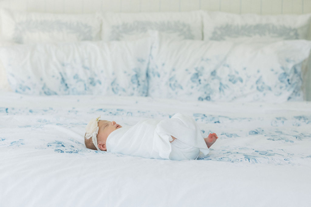 A newborn baby sleeps on a bed in a white swaddle and headband thanks to nannies in new jersey