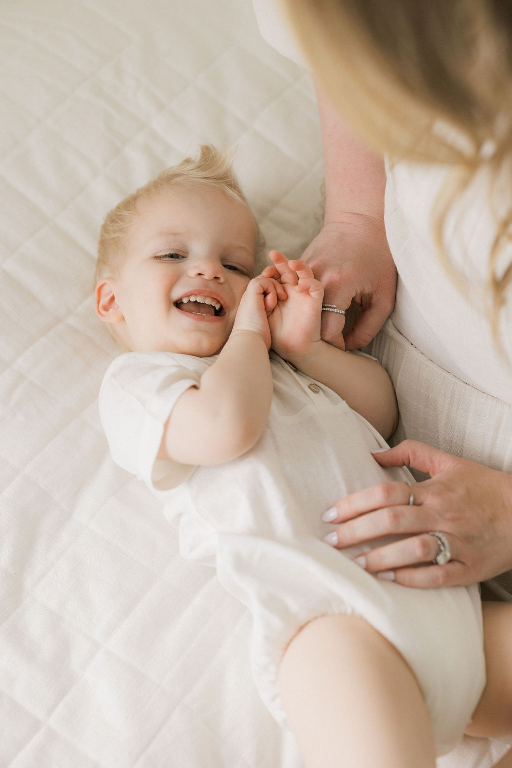 A mom tickles her toddler son on a bed in a studio after using holistic beginnings
