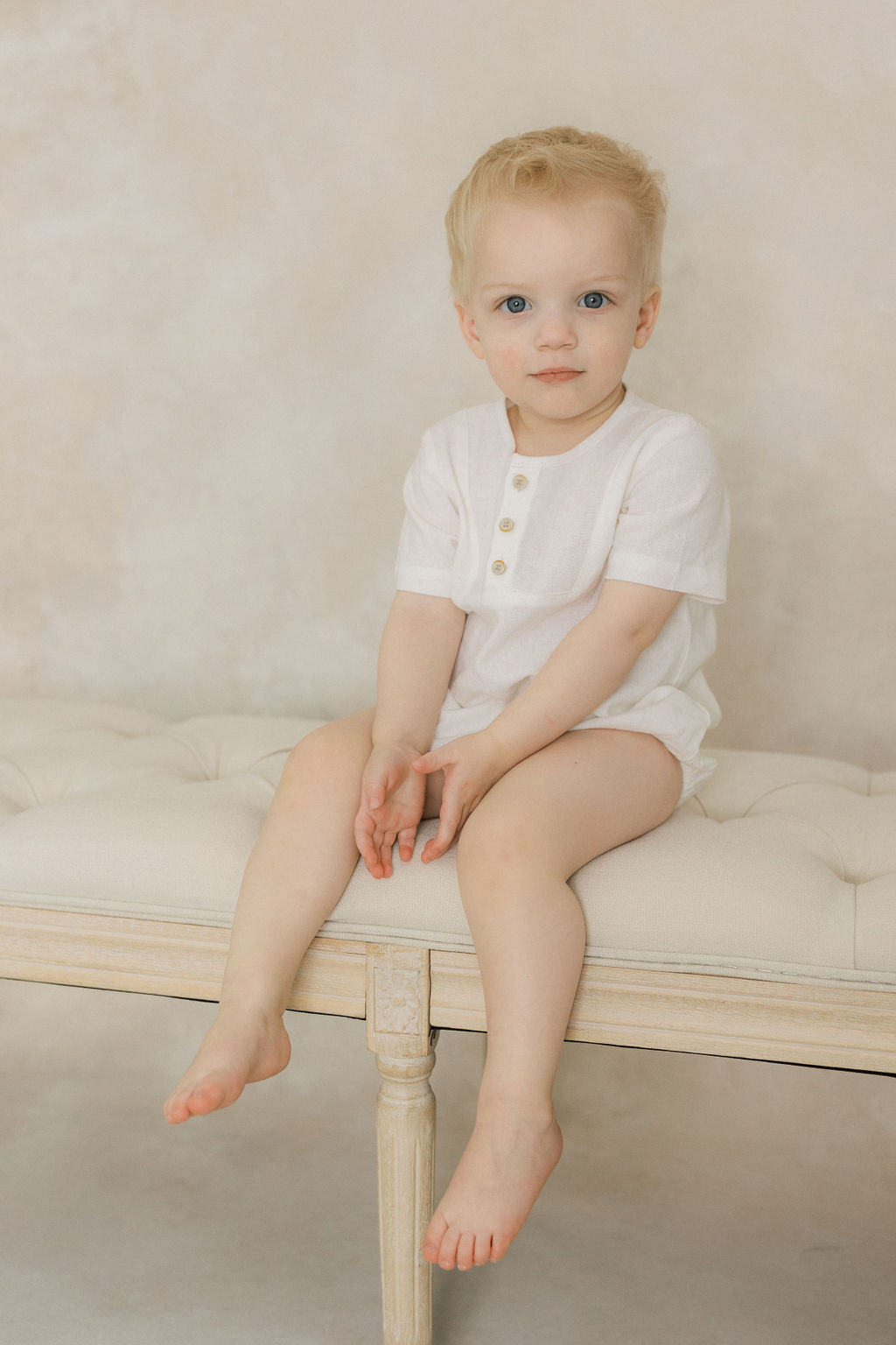 A young toddler boy in a white onesie sits on a bench in a studio thanks to holistic beginnings