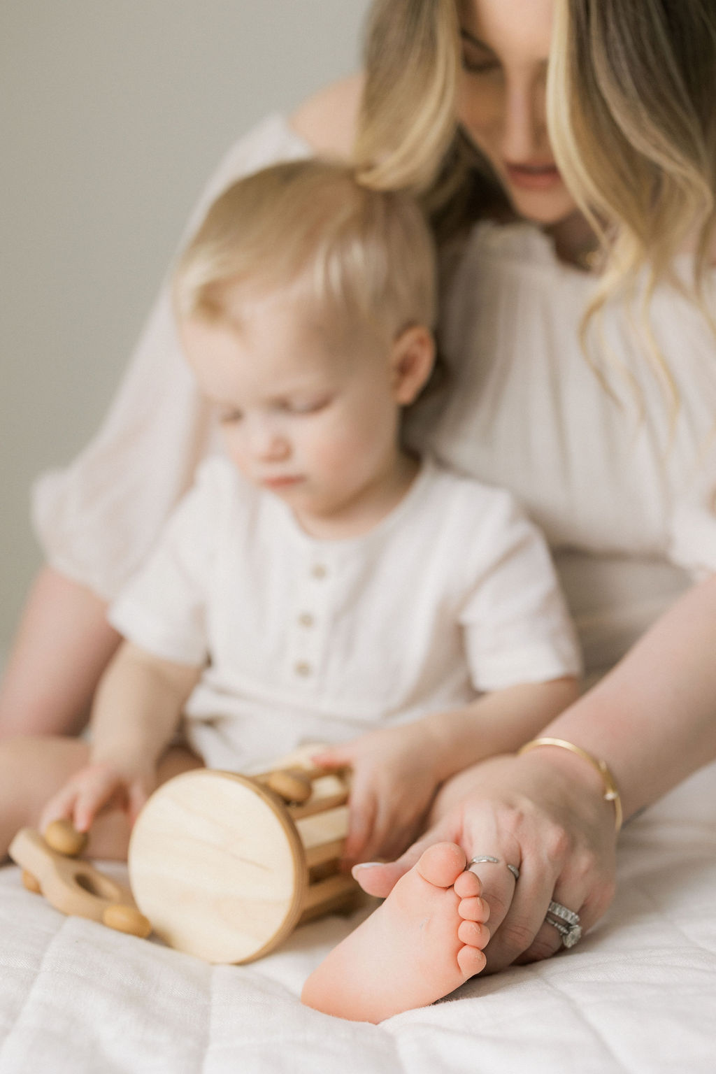 A young boy sits with mom on a bed playing with wooden toys