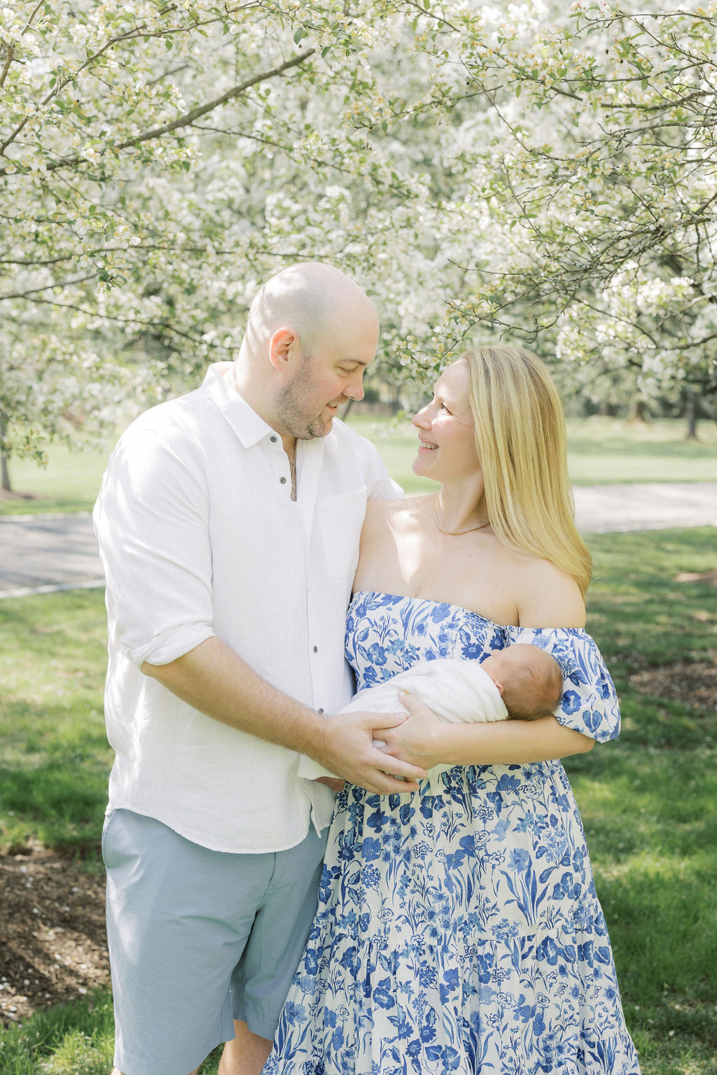 Happy parents stand in a floral park holding their newborn baby in their arms thanks to fertility acupuncture nj