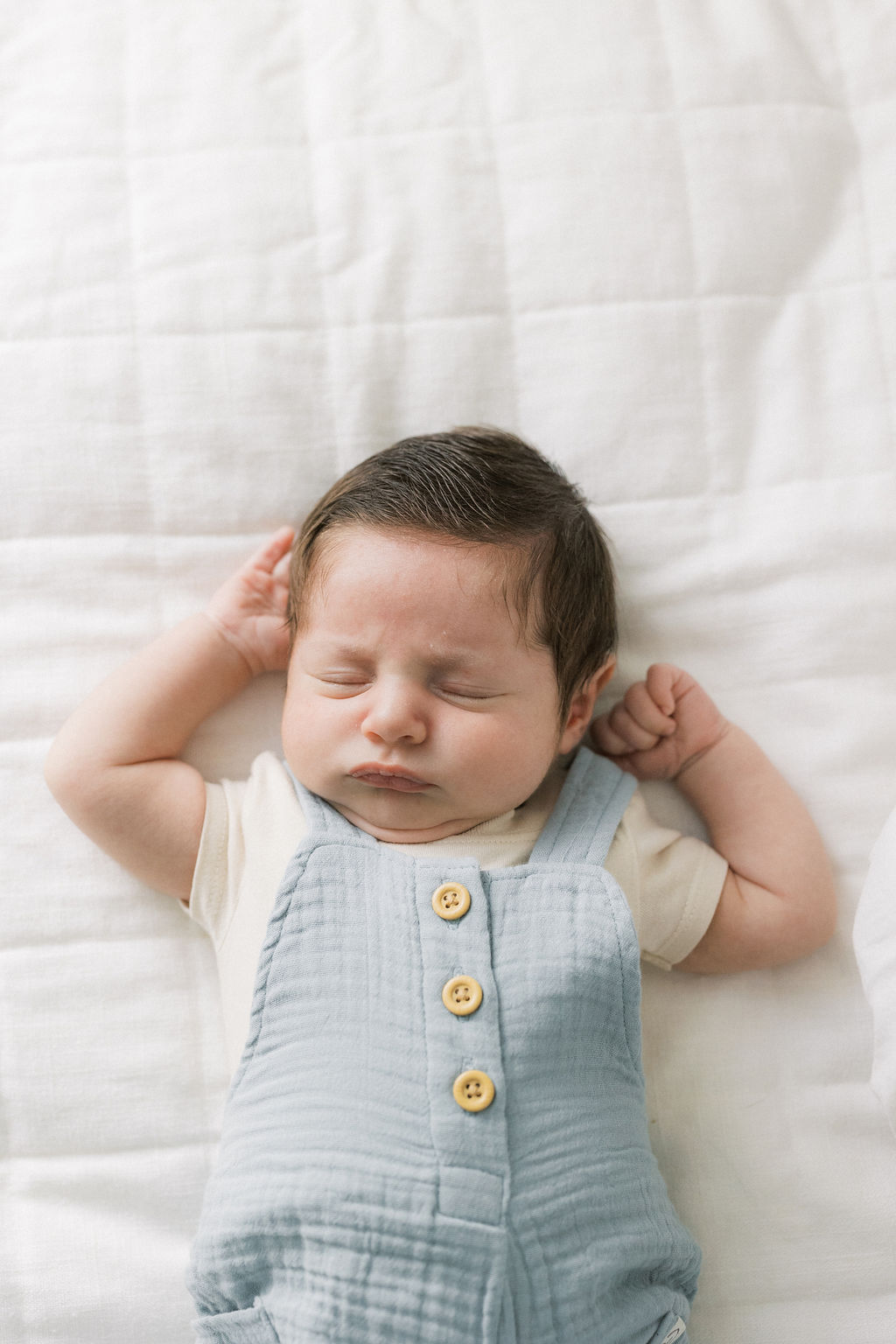 A sleeping newborn baby in blue overalls on a white bed in a studio thanks to support from a 3d ultrasound new jersey