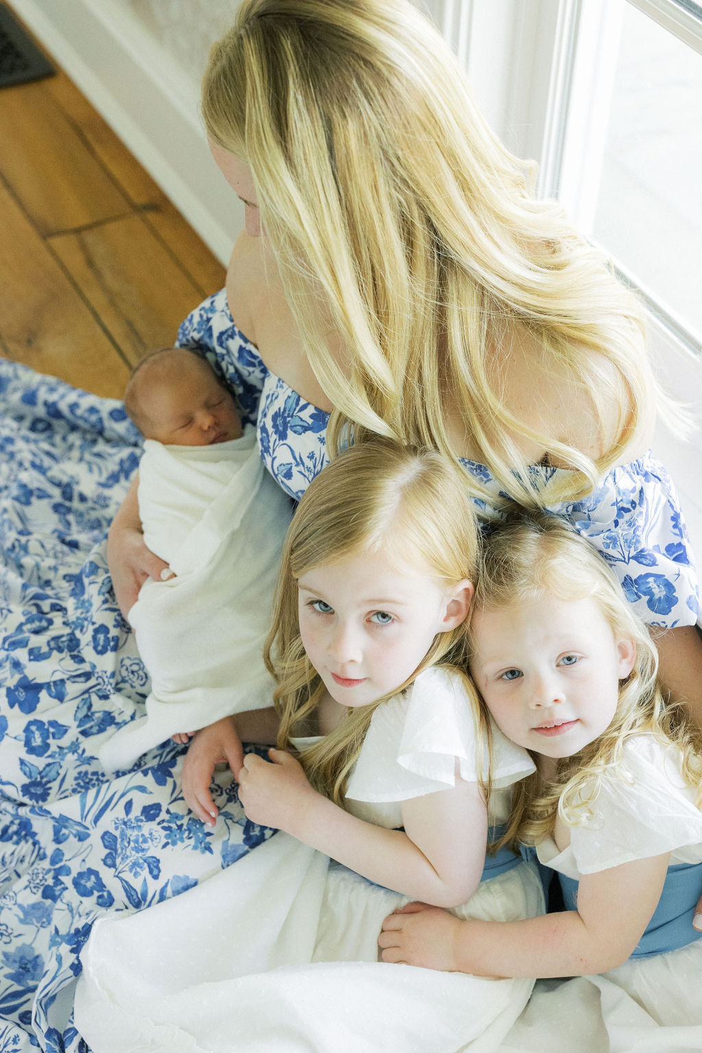 A mother in a blue floral print dress cradles her sleeping newborn baby and two toddler daughters in white dresses before visiting a pediatrician nj