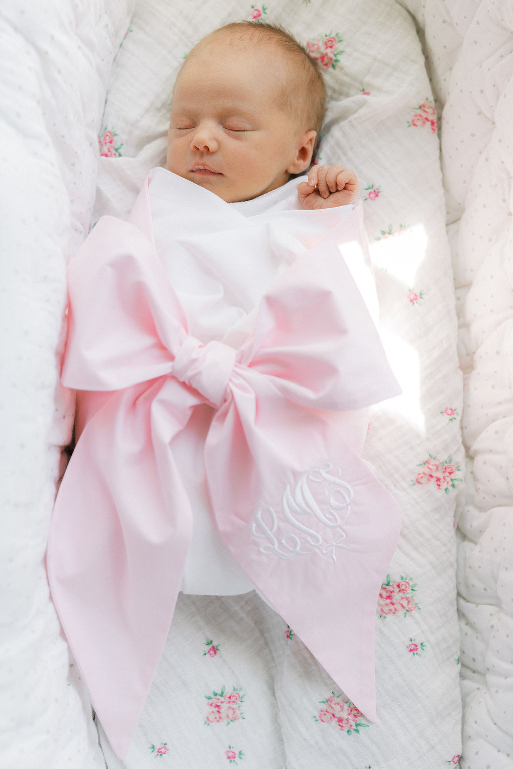 A newborn baby sleeps in a blanketed crib under a large pink embroidered bow thanks to the lactation place