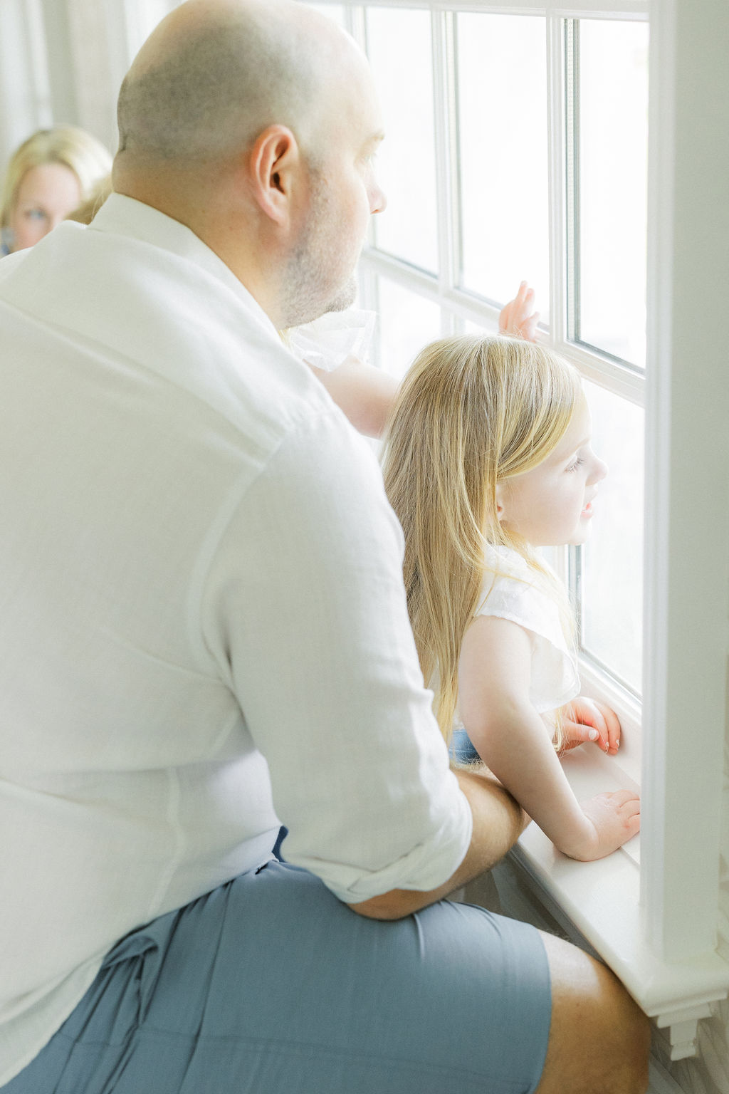 A father gazes out a window with his toddler daughter in his lap