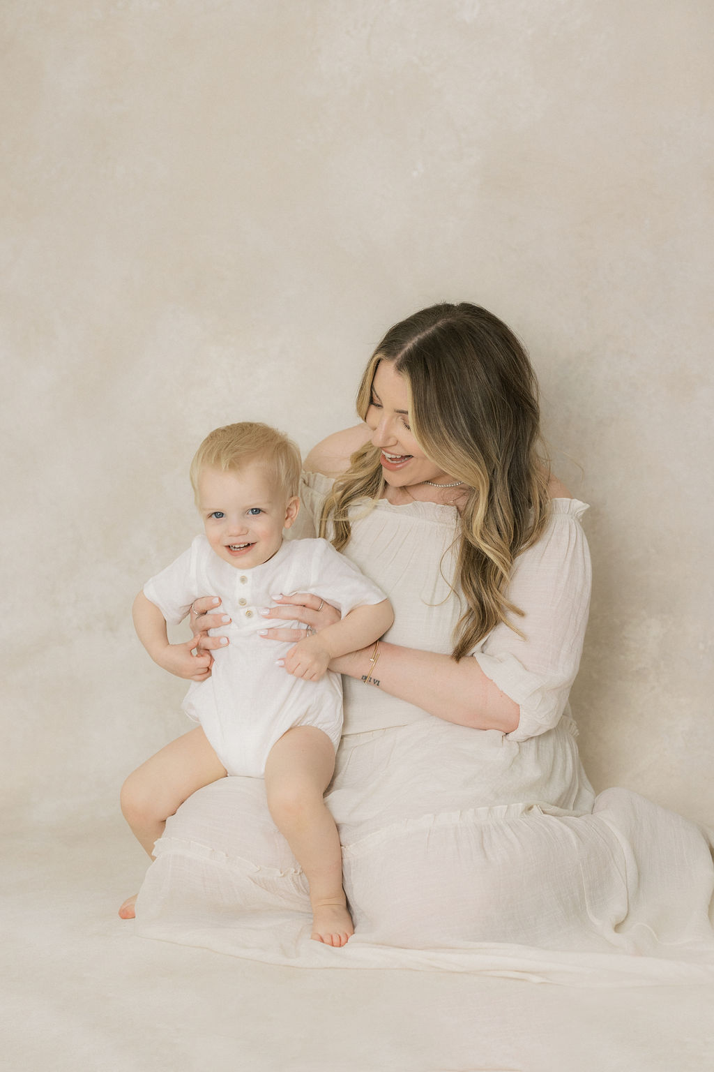 A happy pregnant mom plays with her toddler son in a studio in her lap after some prenatal yoga nj