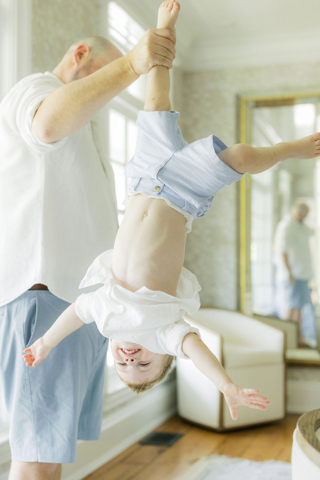 A father dangles his toddler son by the ankle while playing inside before visiting the nest chiropractic